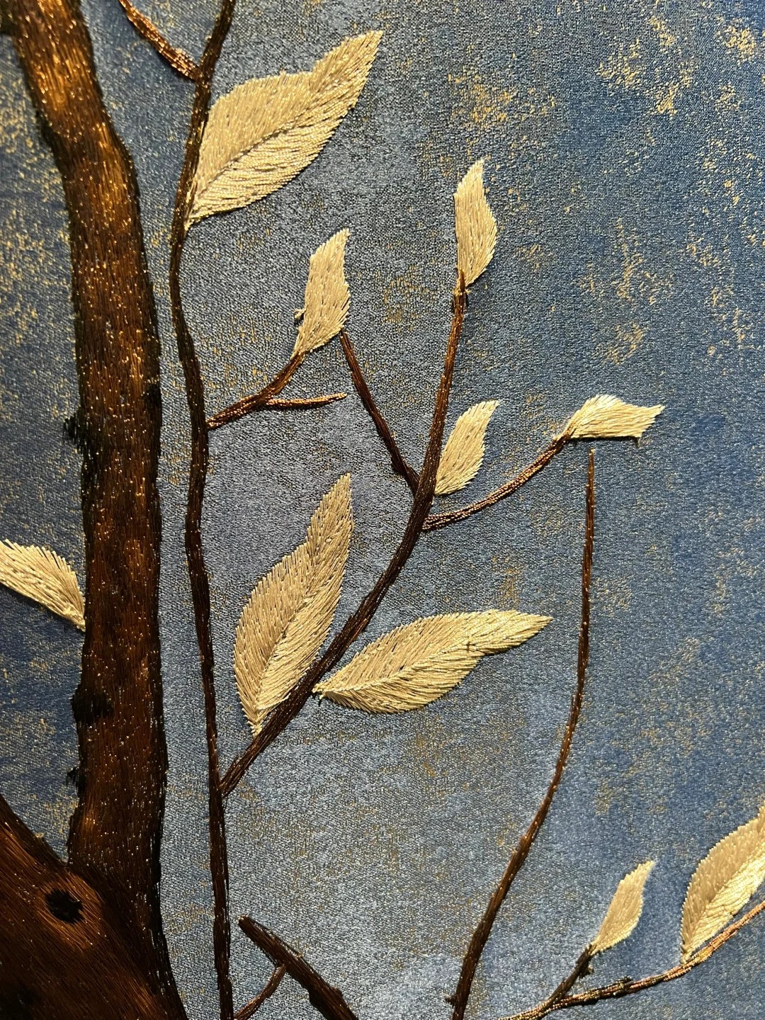 Close-up of embroidered leaf and branch detail on blue textile